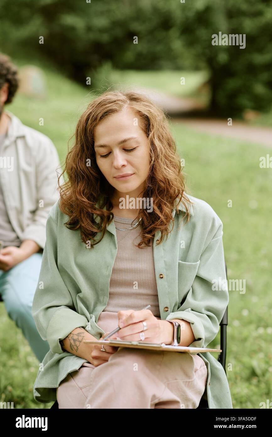 Donna che disegna su una clipboard durante un corso di arte all'aperto Foto Stock