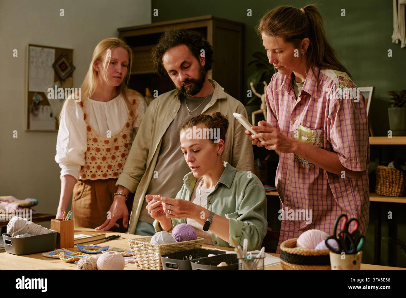 Gruppo di adulti che guardano una donna lavorare a maglia durante un corso di artigianato creativo Foto Stock