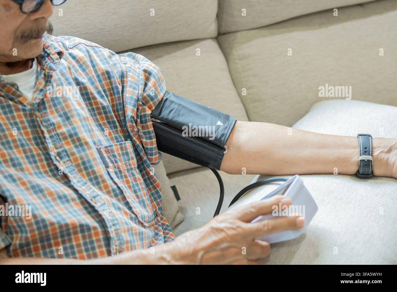 Un uomo anziano pratica l'automonitoraggio con un bracciale per la pressione sanguigna a casa, sottolineando l'importanza dell'assistenza domiciliare e della gestione della salute per gli anziani Foto Stock