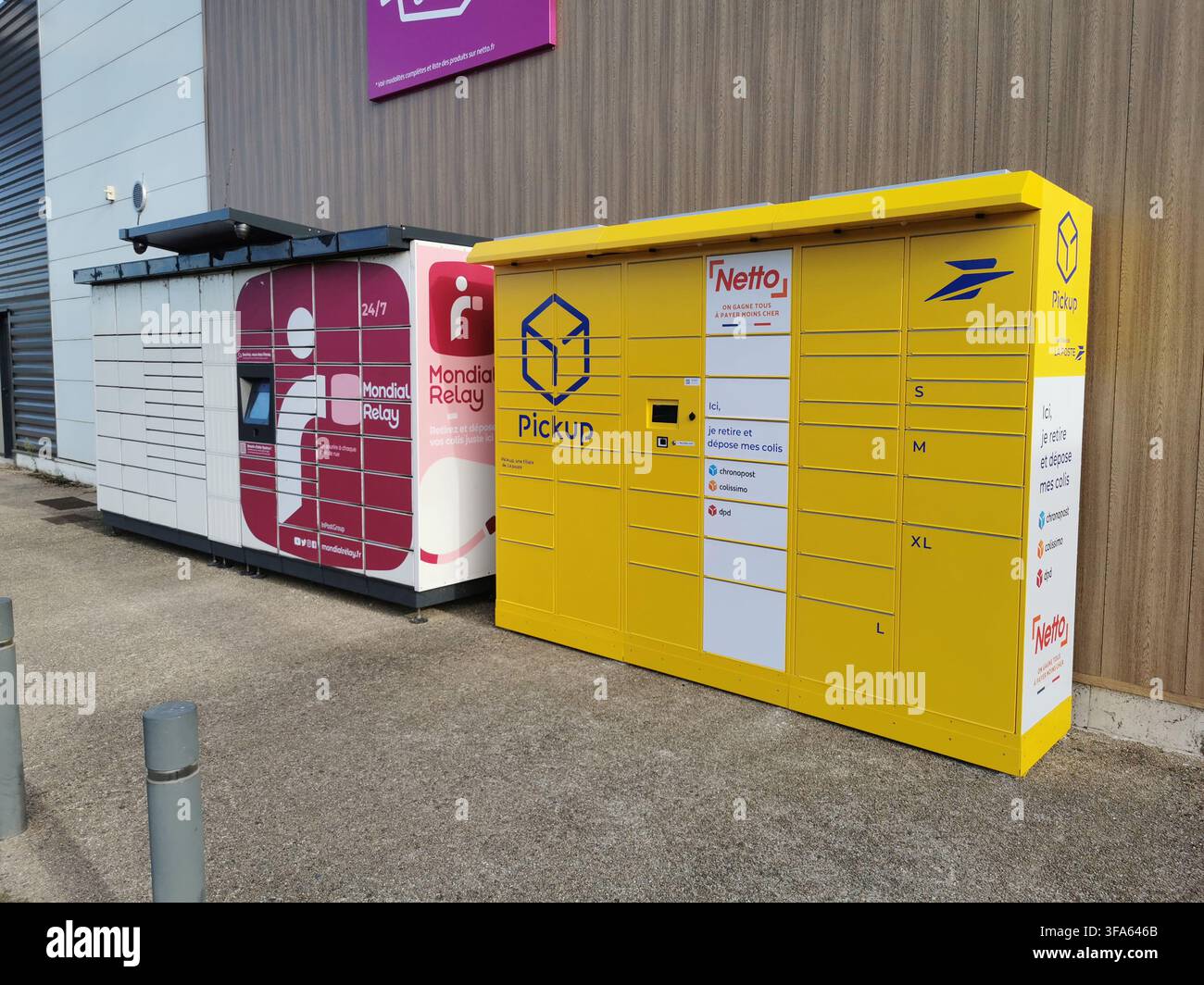 Due armadietti automatici per pacchi, uno rosso e bianco e l'altro giallo, sono posizionati uno accanto all'altro su una superficie lastricata contro il muro di un edificio. Foto Stock