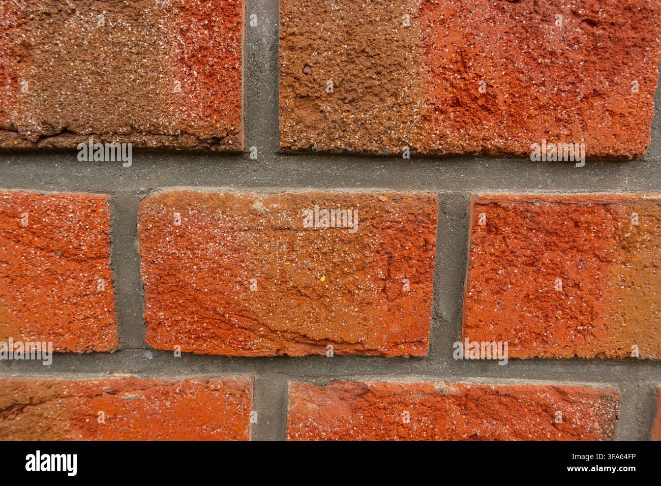 Primo piano di un muro di mattoni rossi consumato che mostra toni arancio-rossi vari, una texture ruvida della muratura e giunti di malta grigi Foto Stock