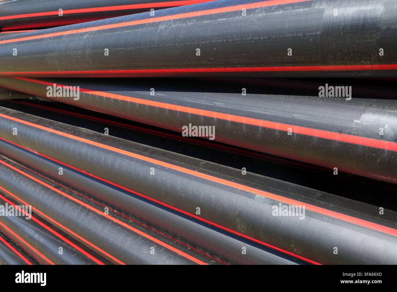 Vengono mostrati tubi in polietilene ad alta densità (HDPE) impilati, tipicamente usati per la protezione dei cavi. I tubi sono neri con strisce rosse distintive che corrono Foto Stock