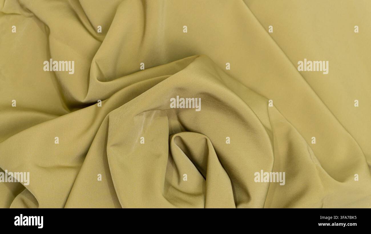 Tessuto verde oliva profondamente stropicciato che forma un motivo centrale a vortice con ombre intense e riflessi luminosi che enfatizzano la texture setosa del materiale. Foto Stock