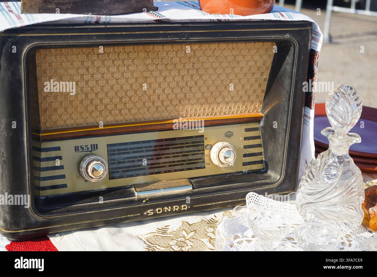 Radiotrasmettitore a valvole vintage "Sonra" esposto accanto a una caraffa di cristallo e una tovaglia ricamata tradizionale. Foto Stock