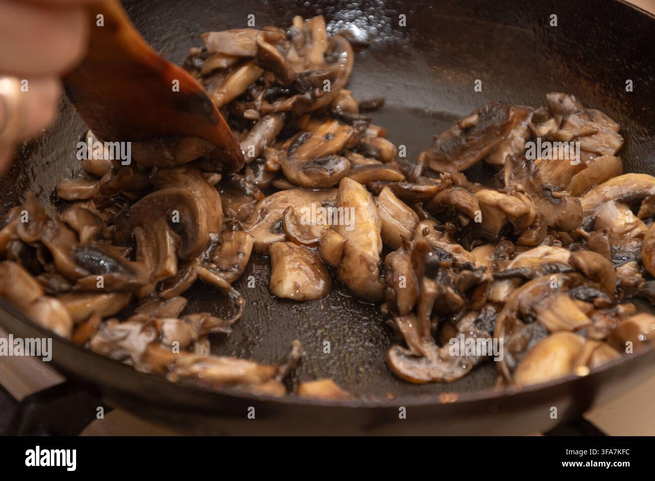 Prima vista di funghi affettati saltati in padella con una spatola di legno. Foto Stock