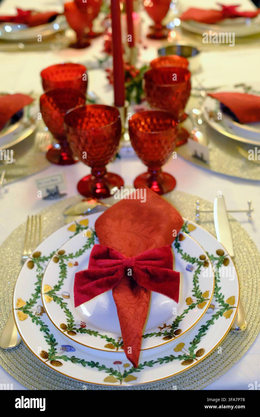 Vista sul lungo tavolo natalizio con bicchieri rossi, candele alte e ambienti eleganti. Foto Stock