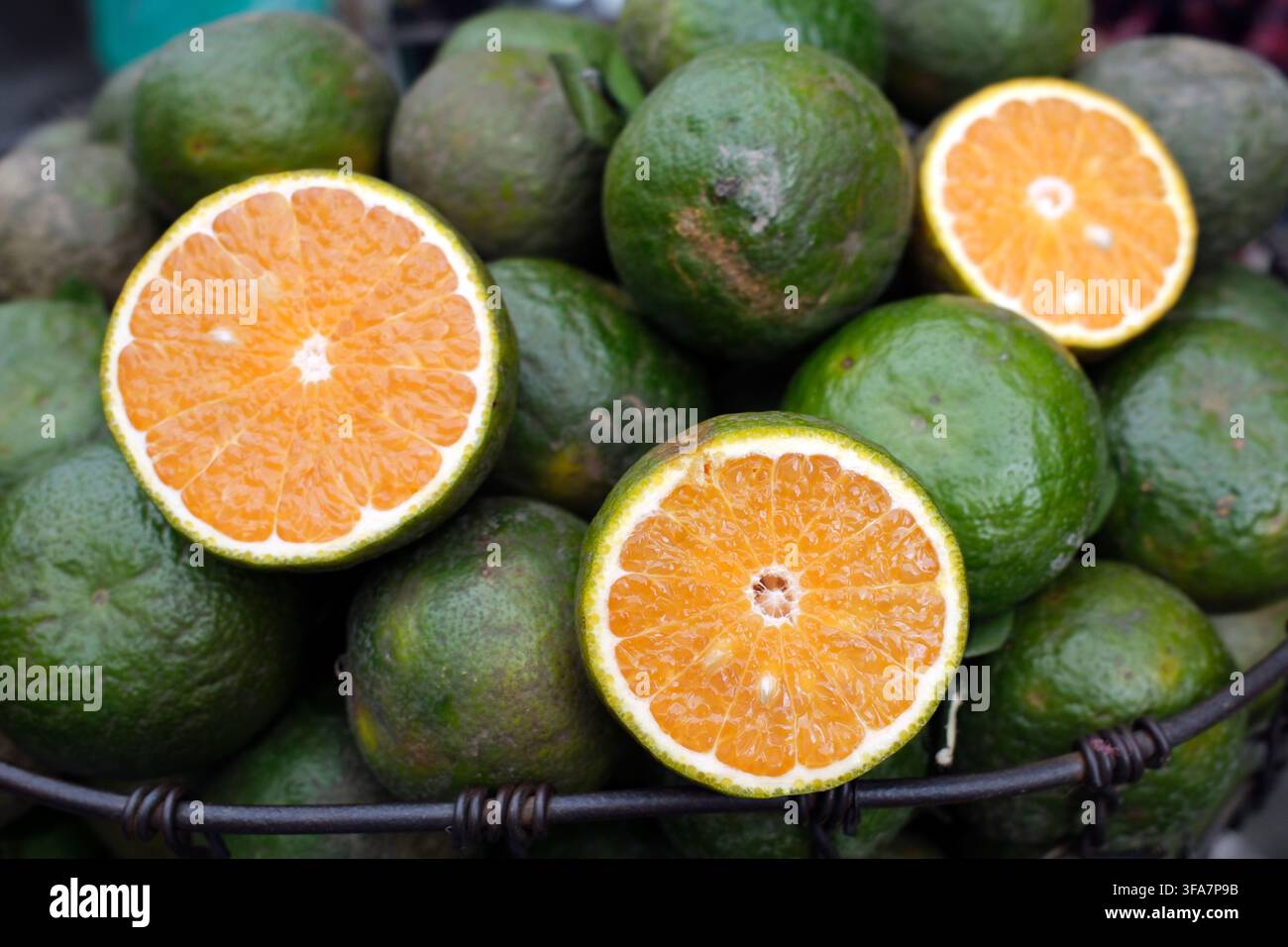 Cesto di arance verdi tagliate a metà in un mercato di strada. Vietnam. Foto Stock