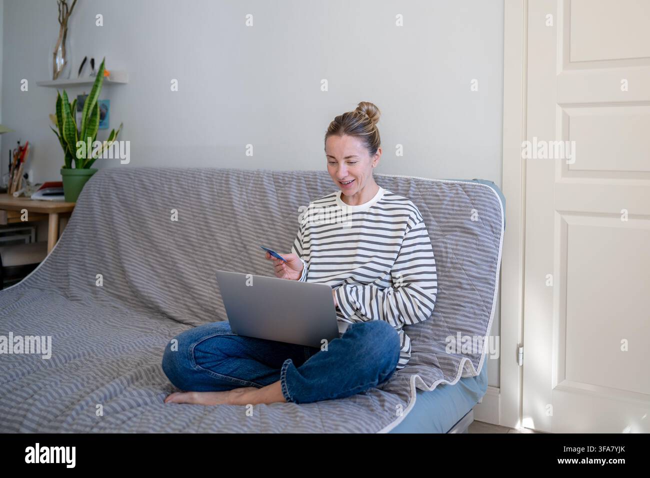 Donna allegra che acquista online su un sito di e-commerce da casa utilizzando un laptop e una carta di credito, Foto Stock