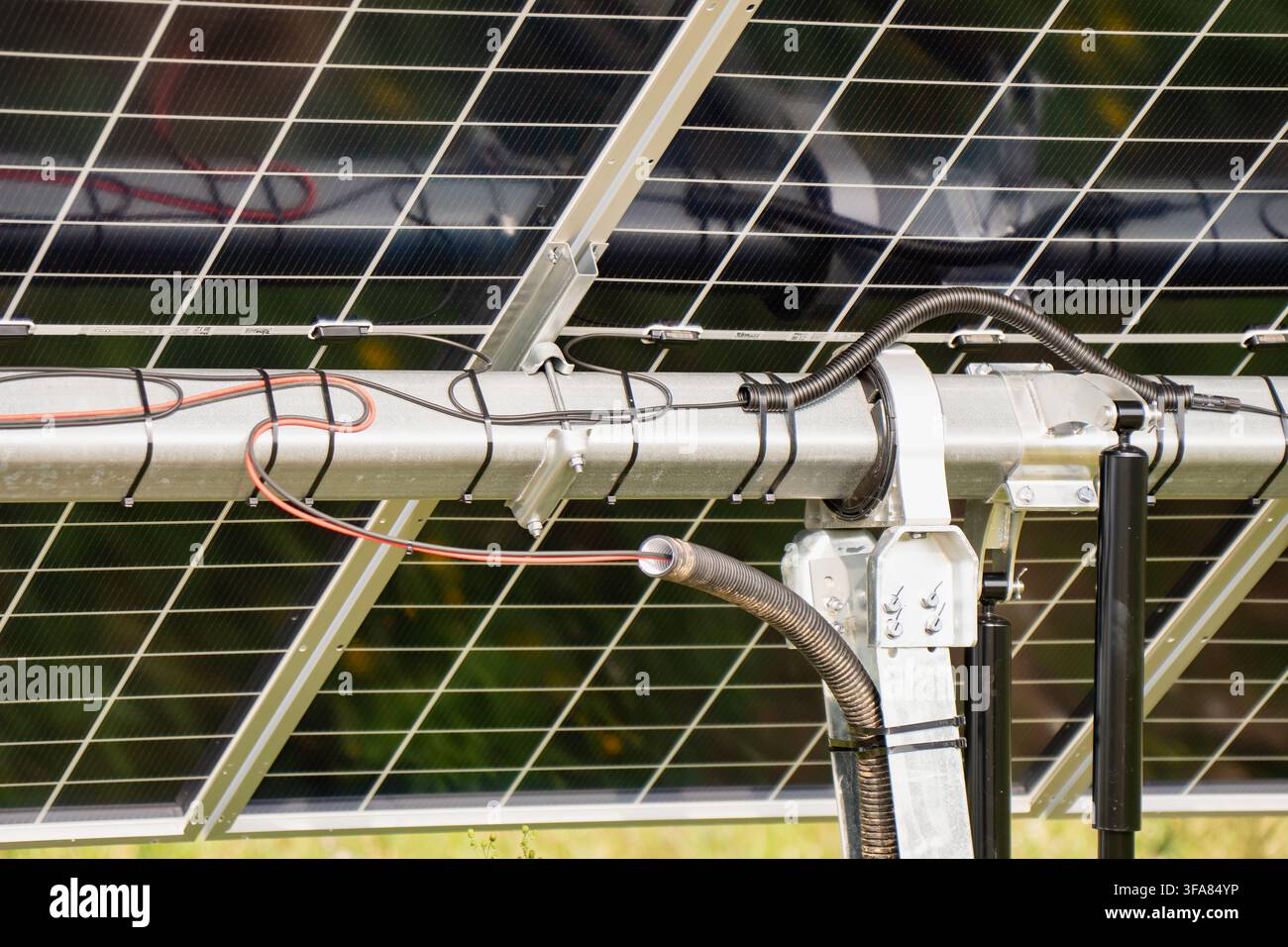 Primo piano di un meccanismo di tracciamento solare a singolo asse con staffa di supporto, ammortizzatori idraulici e percorso del cavo elettrico Foto Stock