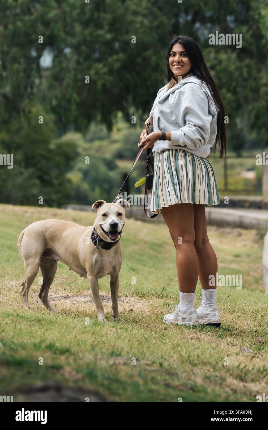 Donna in piedi con il suo cane sorridente al guinzaglio in un parco all'aperto Foto Stock