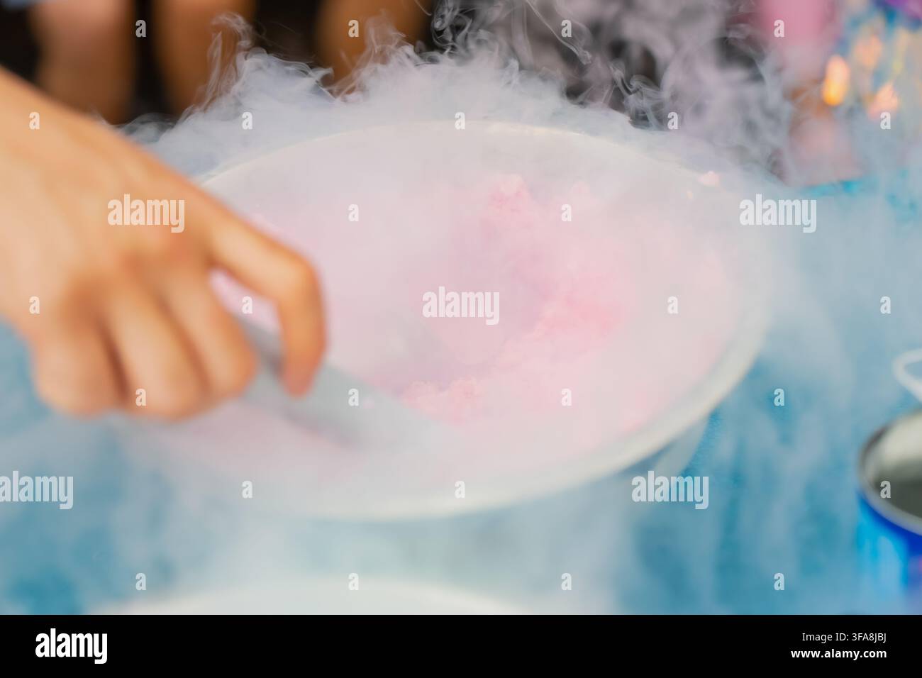 Mano che usa un mestolo di metallo per preparare un dessert gelato rosa congelato con effetto nebbia di azoto liquido in una ciotola in acciaio inossidabile per il catering degli eventi Foto Stock