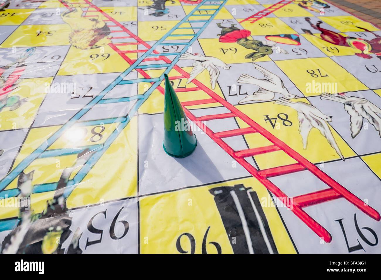 Tappeto da pavimento gigante per il gioco del serpente e delle scale all'aperto con segnaposto a cono verde che rappresenta intrattenimento interattivo, attività ricreative e giochi di gruppo Foto Stock
