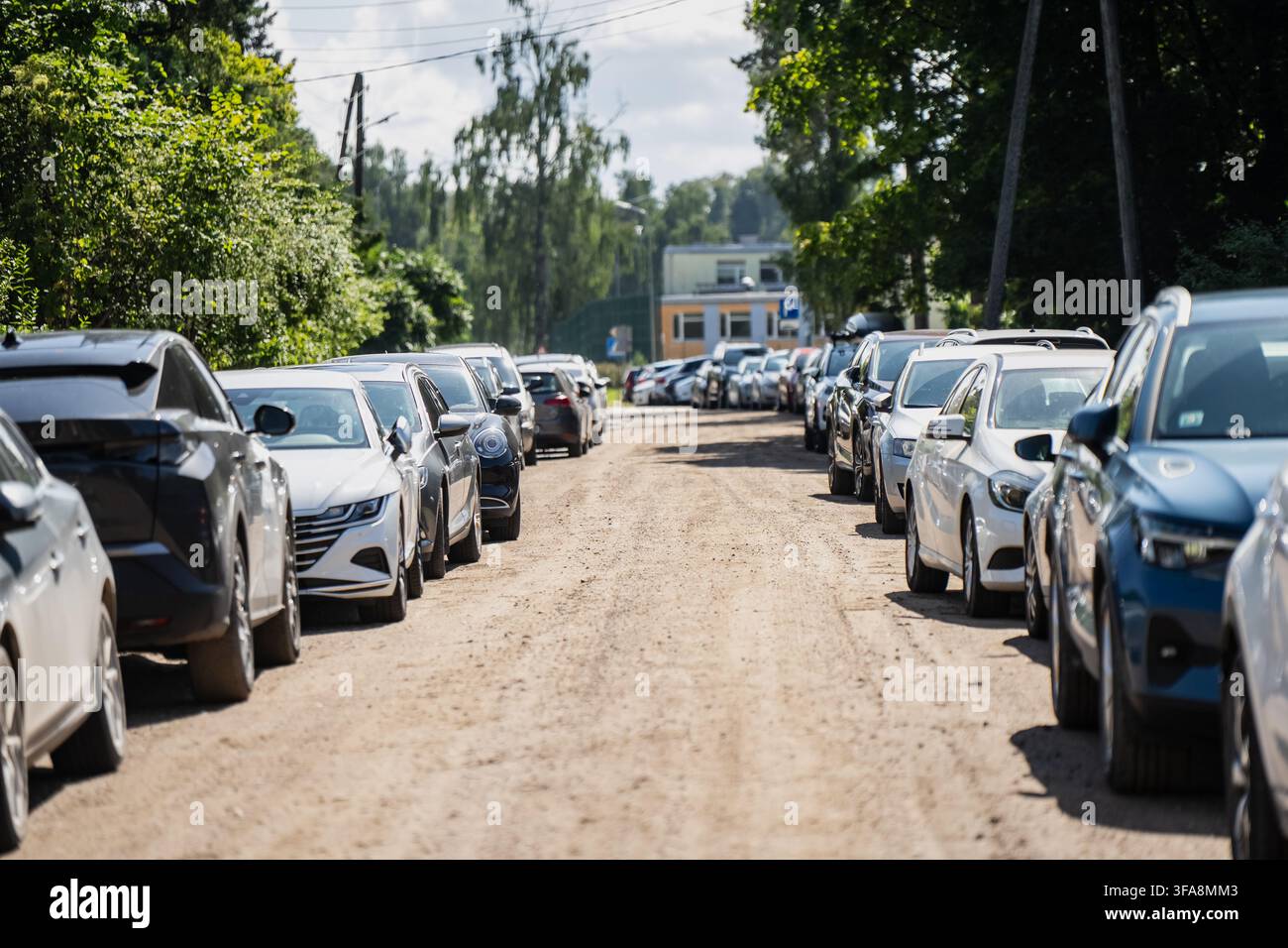 Diverse autovetture parcheggiate lungo entrambi i lati di una strada sterrata non asfaltata che rappresenta il parcheggio suburbano, la gestione del traffico e l'assicurazione auto Foto Stock