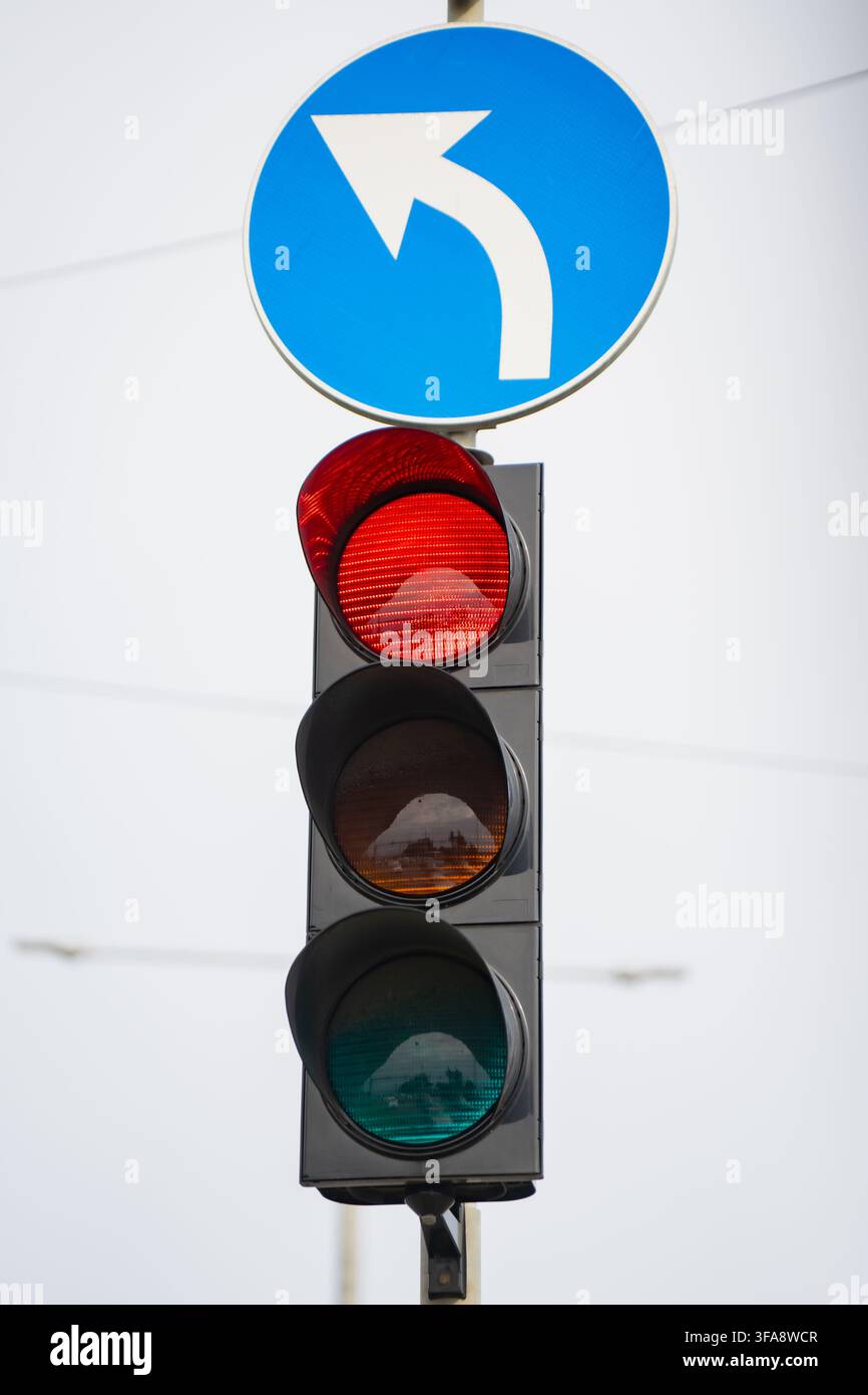 Semaforo con lampada rossa illuminata combinata con un segnale stradale blu di regolamentazione per svoltare a sinistra posizionato sopra il meccanismo di segnalazione Foto Stock