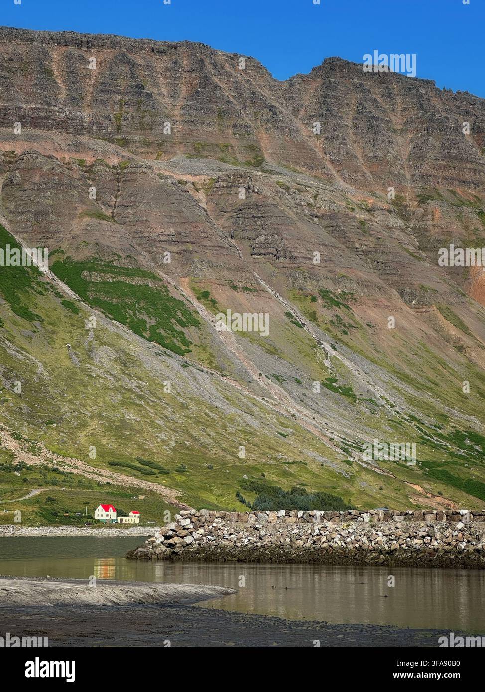 Casa con tetto rosso alla base di una montagna a Isafjordur, Islanda Foto Stock