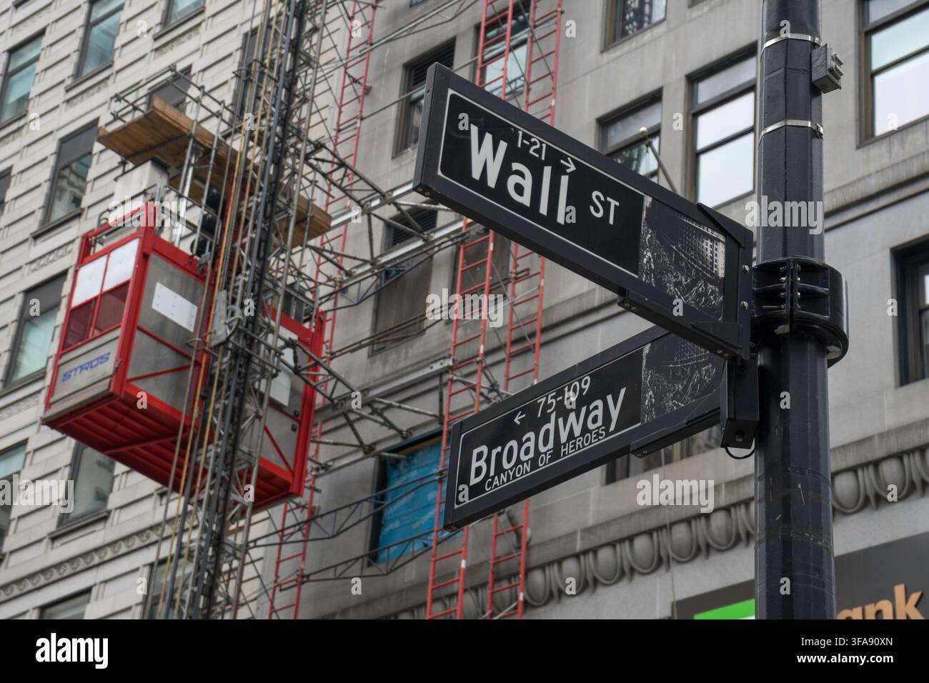 Vista ravvicinata del cartello stradale per l'incrocio tra Wall Street e Broadway con impalcatura di costruzione Foto Stock