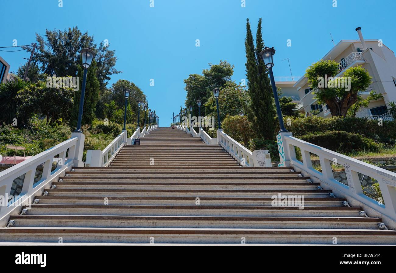 Scalinata in pietra bianca che sale tra aree del giardino e lampioni sotto un cielo blu, Patras, Grecia. Foto Stock