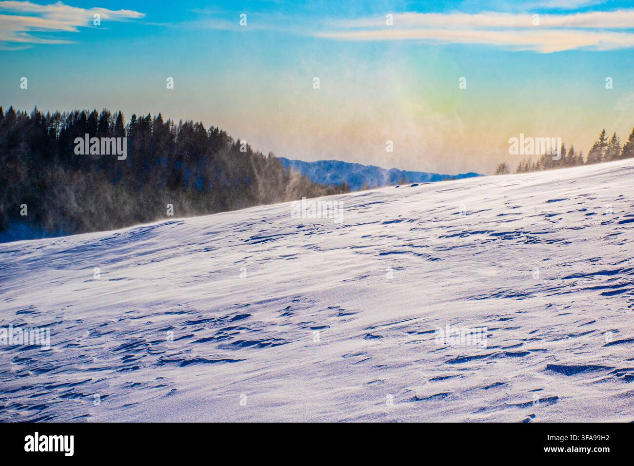 Il vento solleva polvere di neve al tramonto Foto Stock