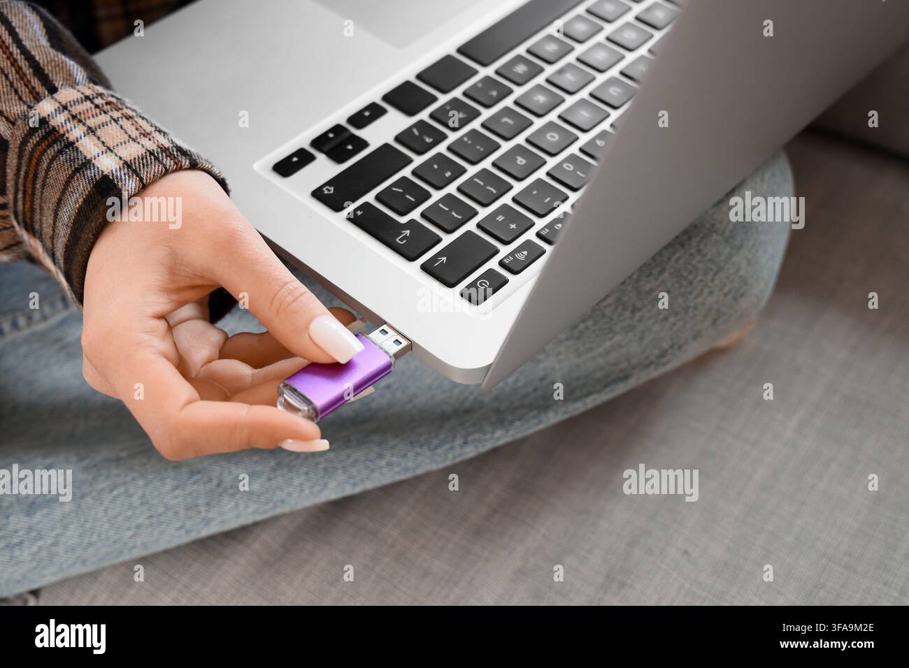Trasferimento di dati e archiviazione digitale, donna che inserisce una chiavetta USB viola nella porta di un computer portatile Foto Stock