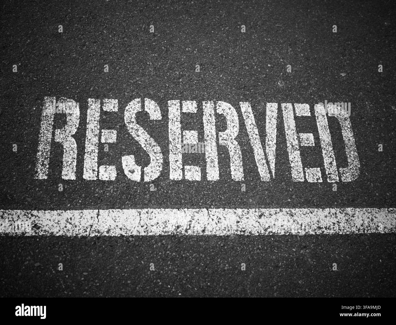 Scrittura RESERVED in stencil bianco su asfalto scuro con linea verniciata bianca. Segnatura generica di parcheggio. Bianco e nero. Foto Stock