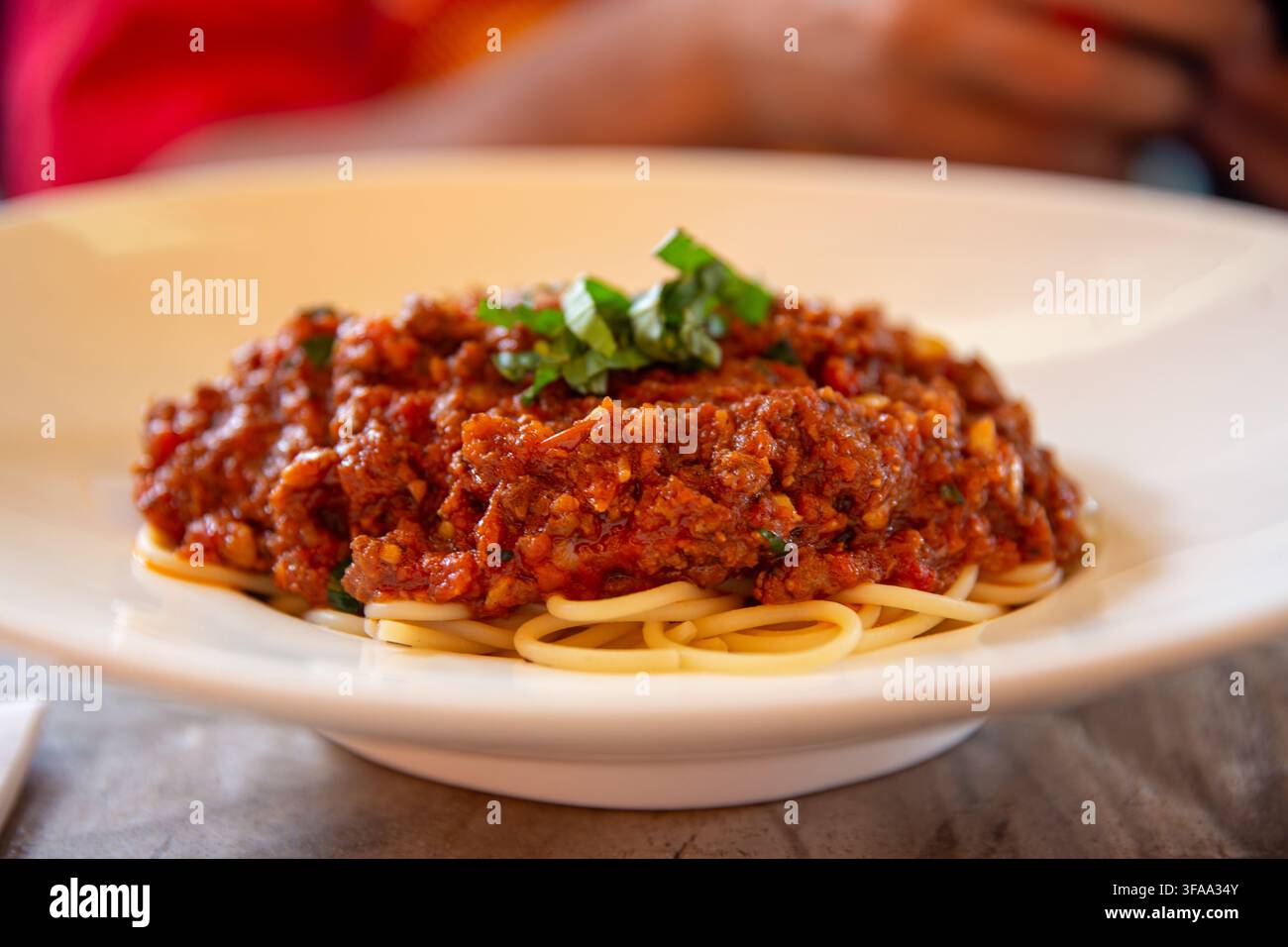 Una vista ravvicinata di un piatto di spaghetti appena servito, ricoperto da una generosa porzione di ricca e densa salsa bolognese e guarnito con trito Foto Stock