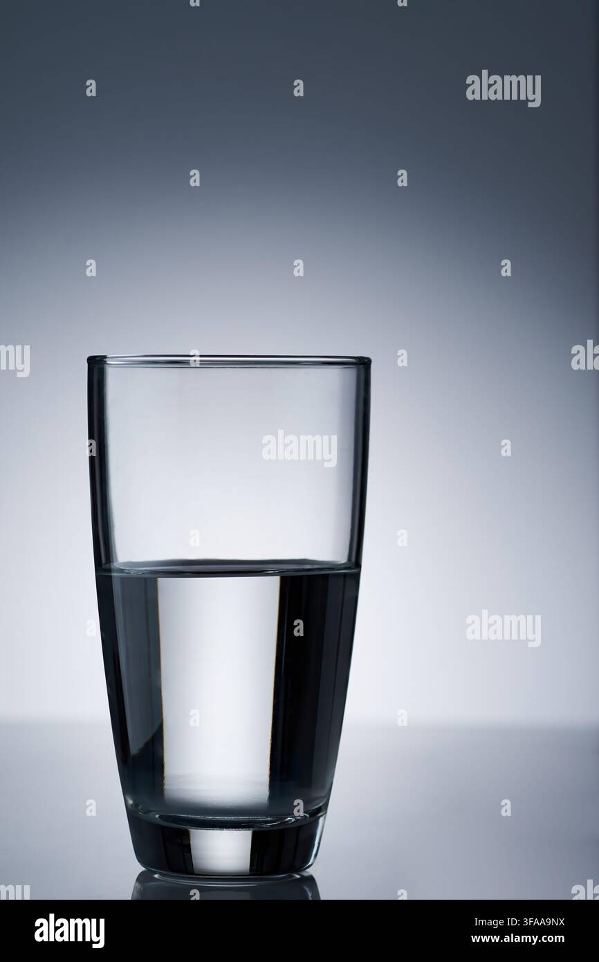 un bicchiere alto e trasparente riempito a metà con acqua potabile su uno sfondo luminoso bianco chiaro e con vignetta scura Foto Stock