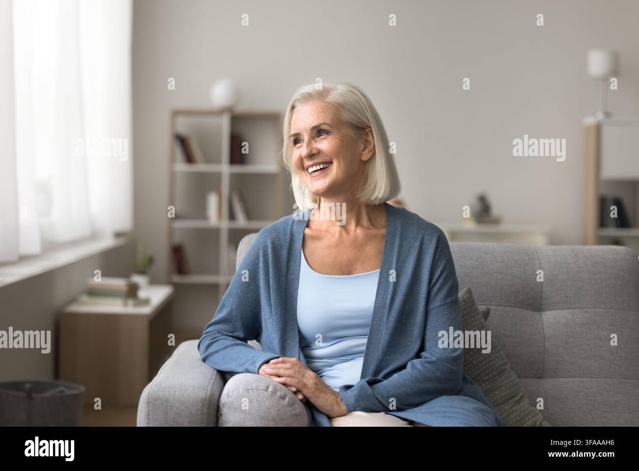 Anziana sorridente felice si rilassa sul divano in salotto Foto Stock