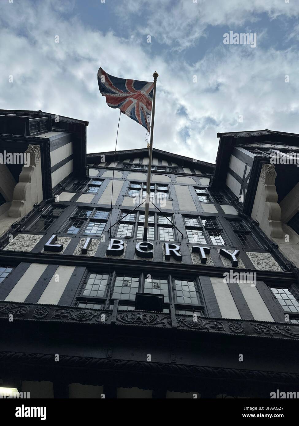 Vista a bassa angolazione della facciata in stile Tudor revival del grande magazzino Liberty London con il cartello illuminato e la bandiera Union Jack. Londra, Regno Unito. - Immagine stock catturata con smartphone