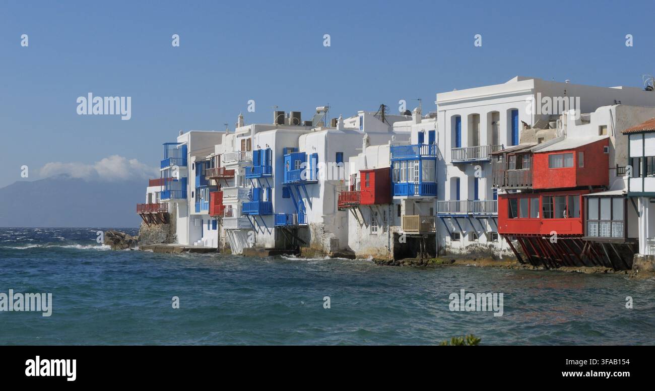 Vista del caratteristico lungomare di Little Venice con i suoi edifici bianchi tradizionali, i balconi vivaci blu e rossi e i supporti in legno sopra l'Egeo Foto Stock