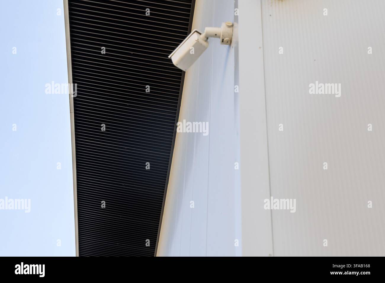 Una telecamera di sorveglianza bianca è attaccata all'esterno di un edificio moderno con una facciata bianca a costolature Foto Stock