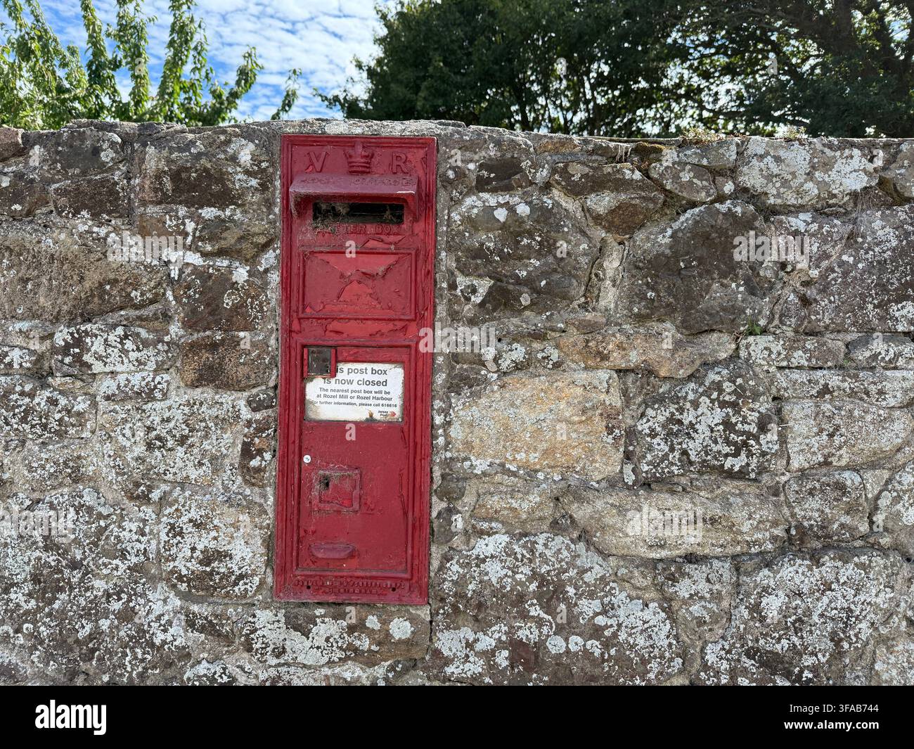 JERSEY, ISOLE DEL CANALE – 04 agosto 2025: Una tradizionale cassetta postale rossa incassata in un muro di pietra reca un avviso che indica che è ora chiusa e non più in - Immagine stock catturata con smartphone