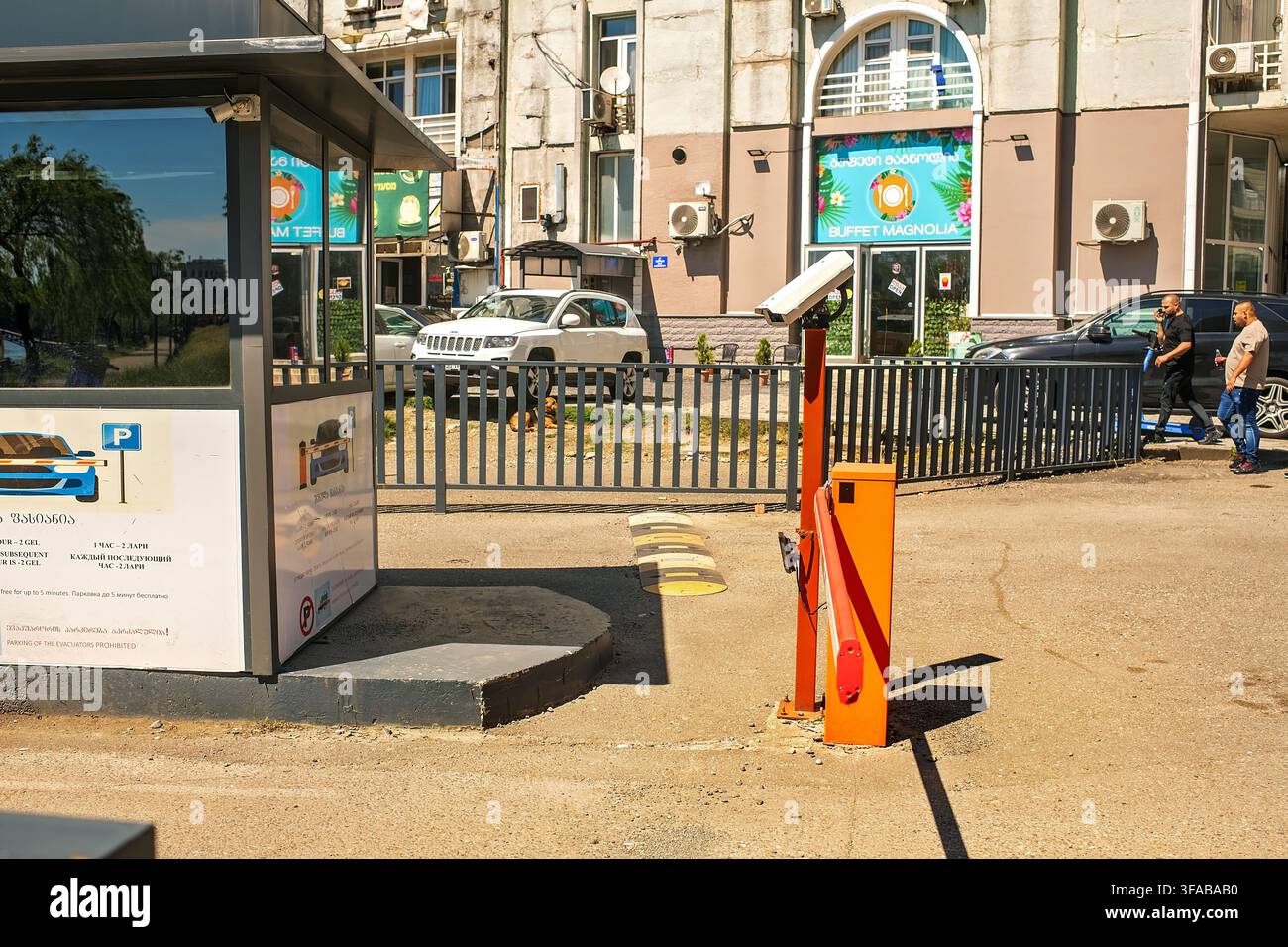 Batumi, Georgia - 19 luglio 2026: Barriera automatica per parcheggio con cabina, telecamera di sicurezza e dossi sulla strada cittadina soleggiata vicino alla facciata di un edificio. Foto Stock