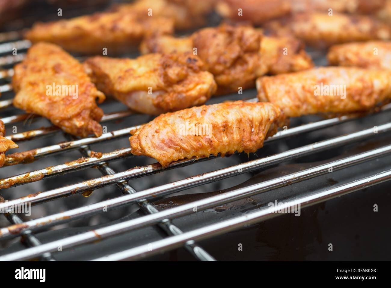 Vista ravvicinata di ali di pollo condite che cuociono e arrostiscono su una griglia metallica del barbecue sopra un fuoco di carboni ardenti durante un pasto nel weekend in giardino. Foto Stock