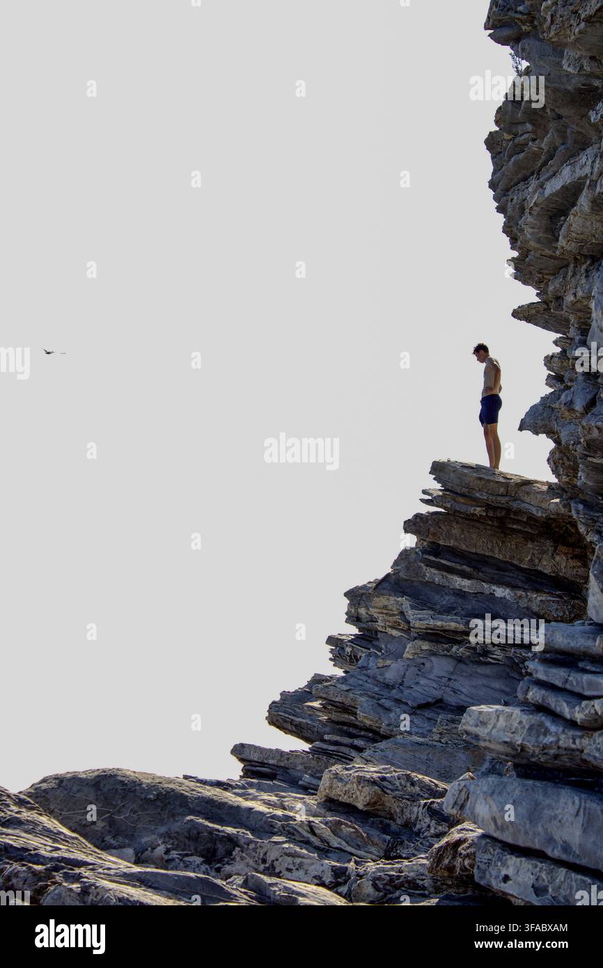 Giovane uomo in piedi sul bordo di una ripida scogliera rocciosa che si prepara a saltare nel mare sottostante Foto Stock