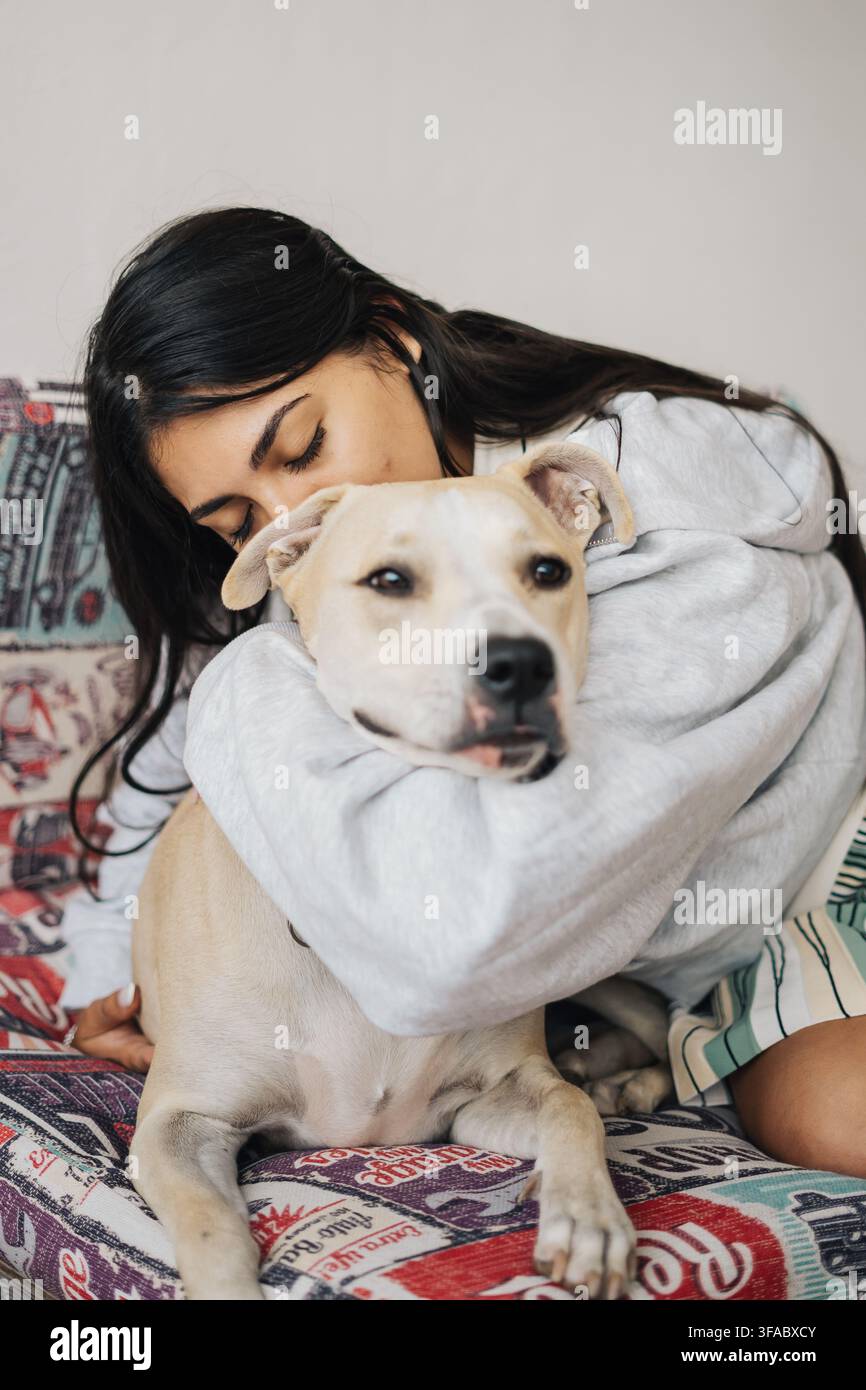 Donna che abbraccia il suo cane su un divano colorato, condividendo un momento d'amore Foto Stock