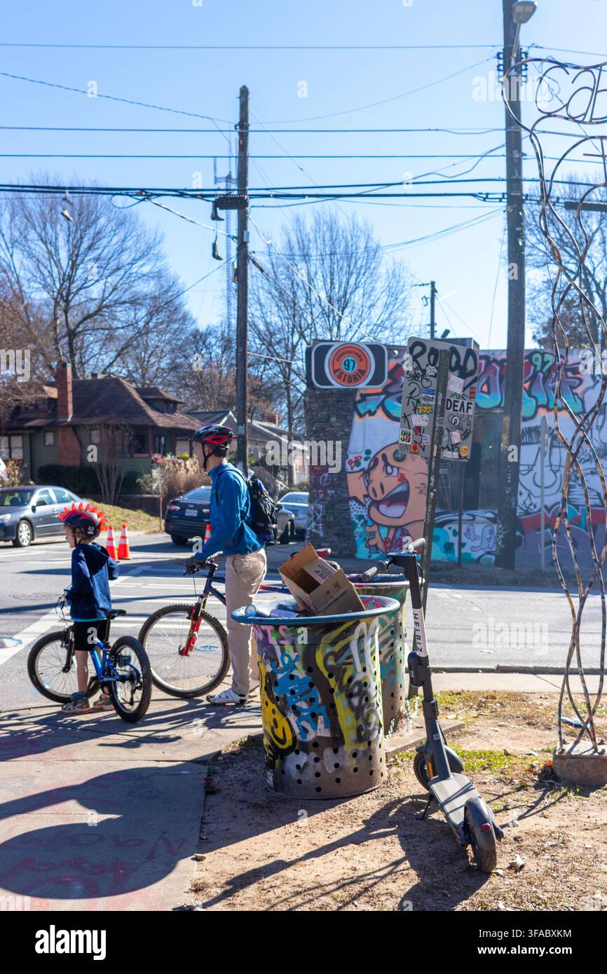 Atlanta, Georgia, Stati Uniti - 18 gennaio 2021: Vista di un uomo e un bambino in bicicletta in attesa a un angolo di strada con un bidone della spazzatura coperto di graffiti Foto Stock