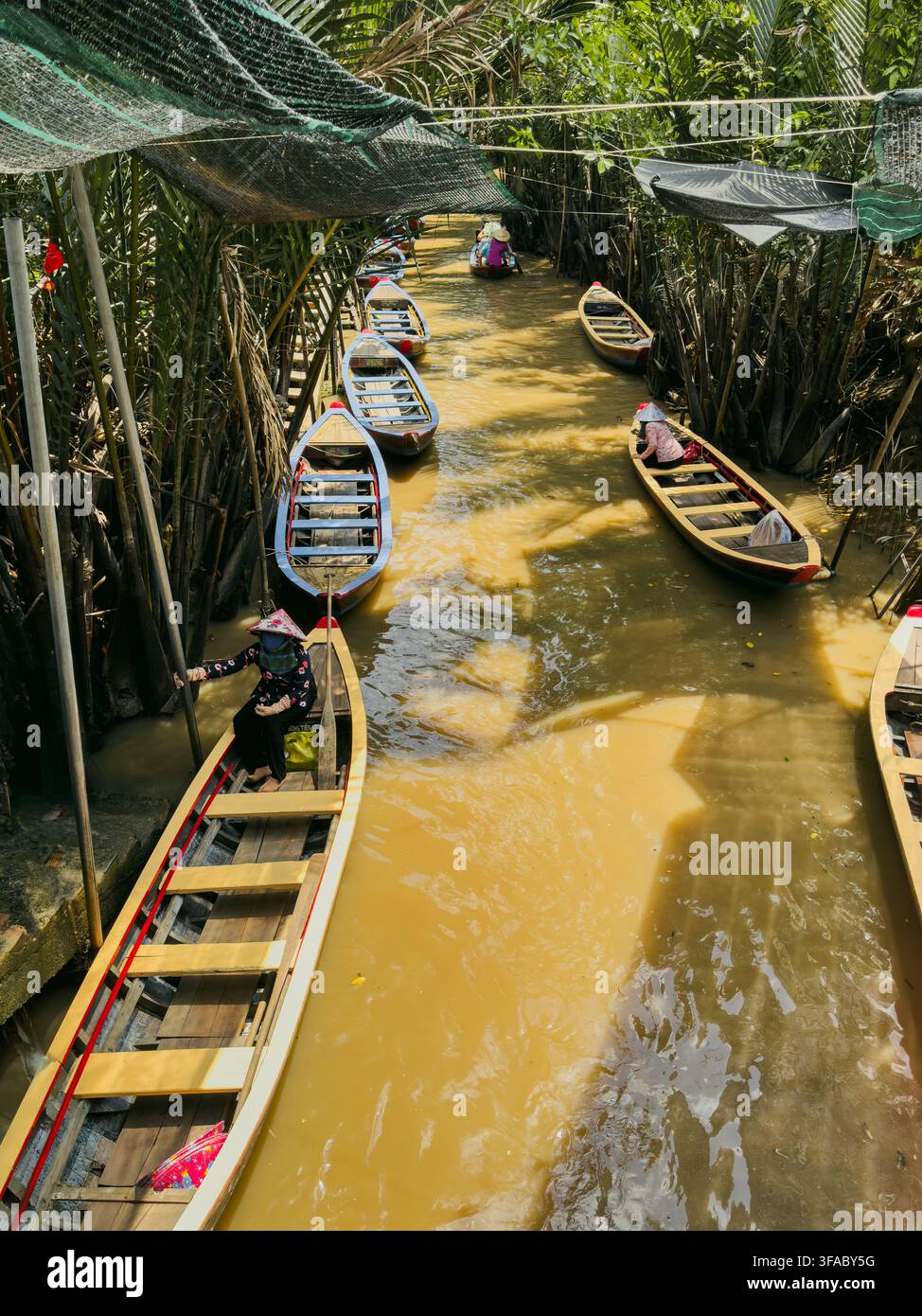 Vietnam - 17 agosto 2026: Vista di barche di legno tradizionali che navigano in un canale stretto del Delta del Mekong, con gente del posto che indossa cappelli a cono sotto Foto Stock