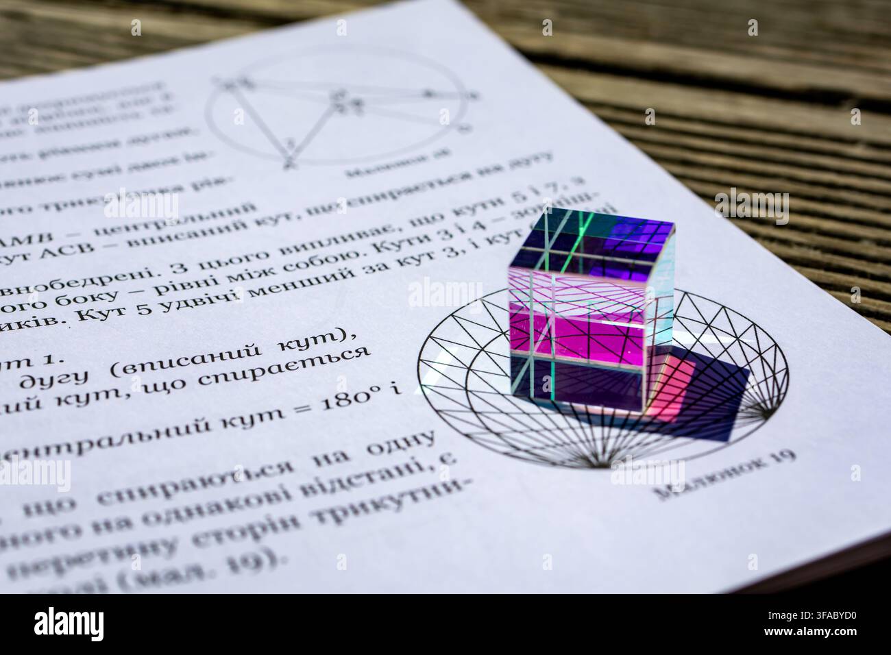 Un cubo di dispersione con riflessi vibranti si trova su una pagina di matematica con una costruzione circolare radiale che fonde ottica e geometria per un giocoso ma ri Foto Stock