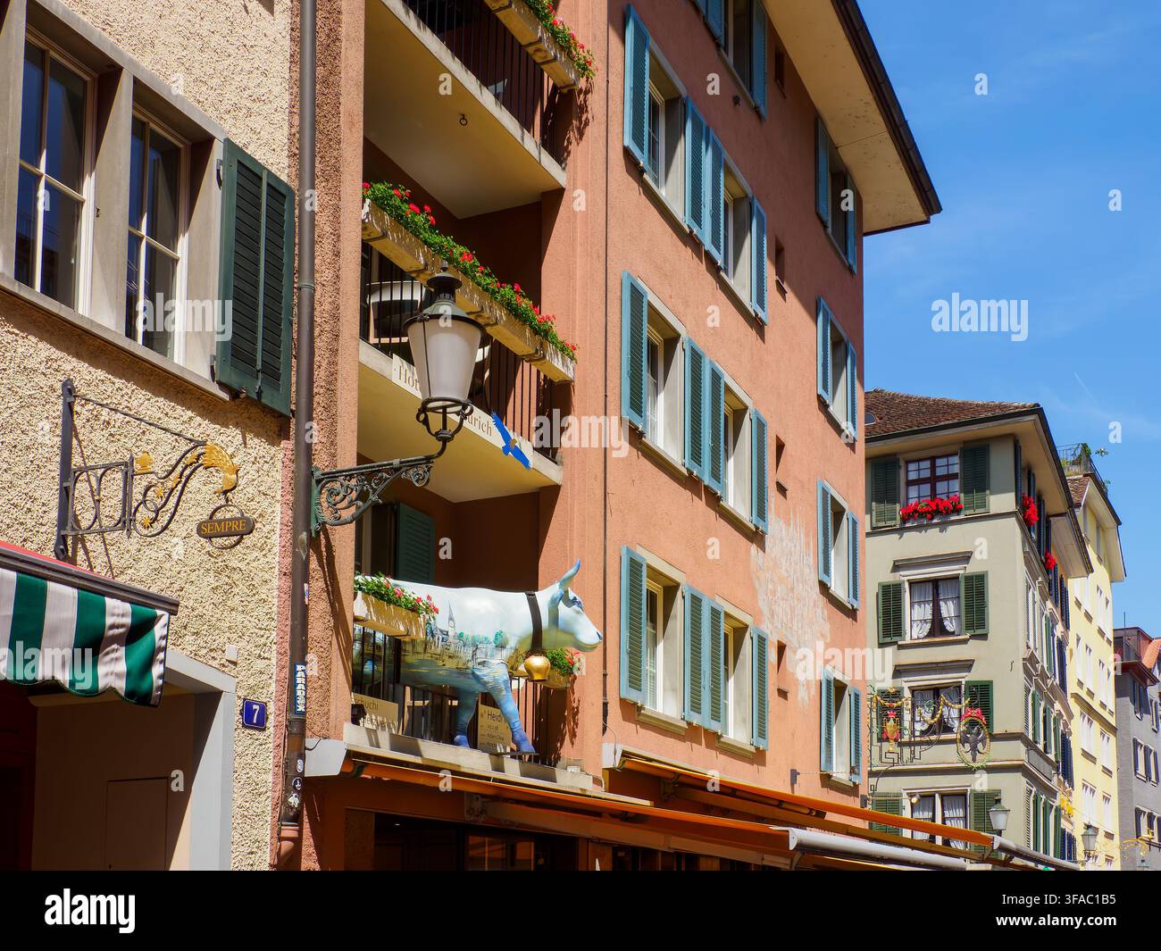 Un edificio a Zurigo sembra ospitare una mucca bianca vista su un balcone sopra il ristorante sottostante Foto Stock