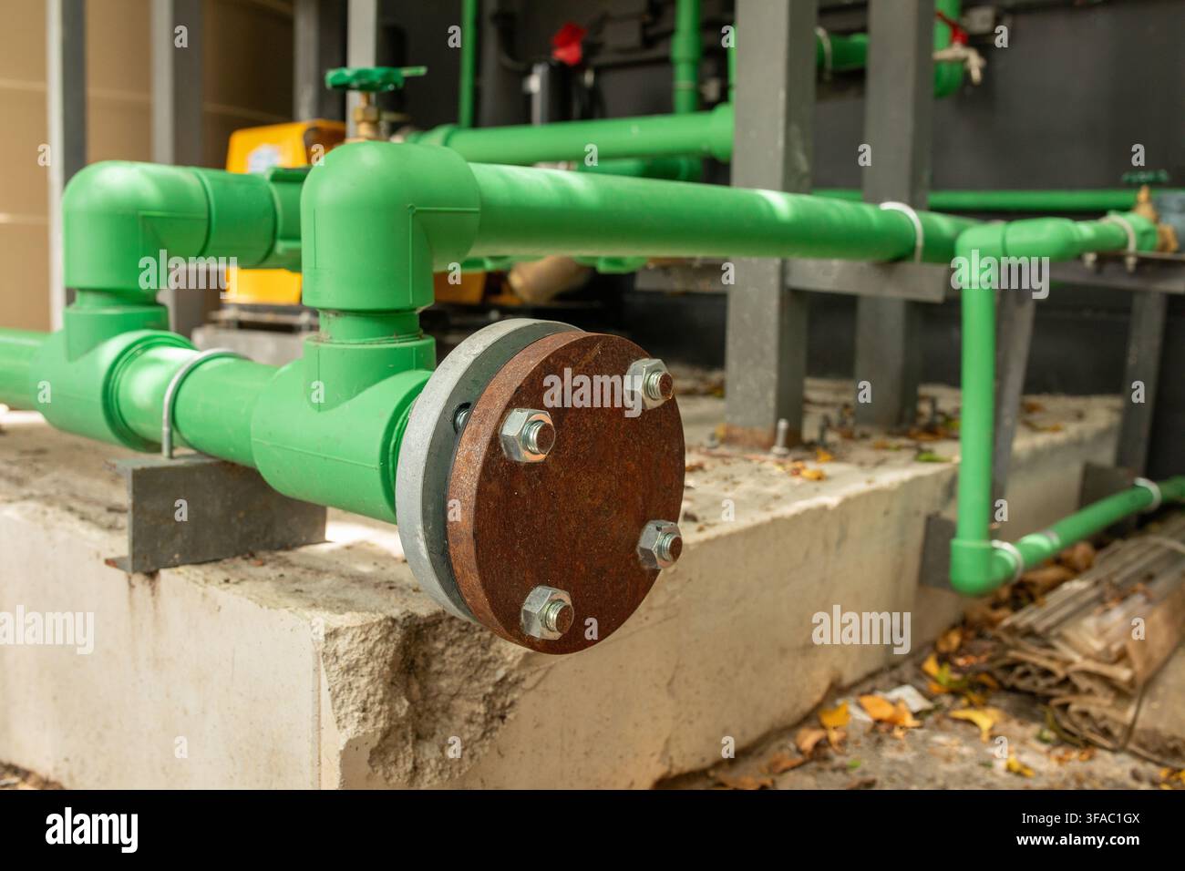 Tubi in PVC verdi collegati con giunto a flangia arrugginito montati su base di cemento vicino all'edificio, dettaglio dell'infrastruttura idraulica Foto Stock
