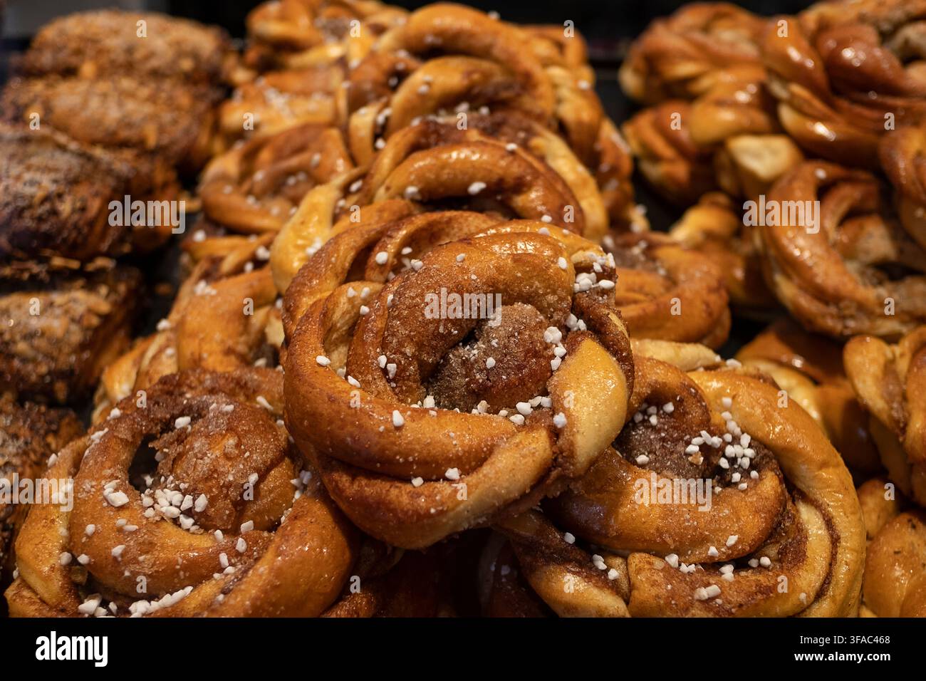 Rotoli di cannella tradizionali scandinavi freschi disposti in una vetrina di panetteria, pasticcini dorati ricoperti di zucchero perlato, ripieni di spezie aromatiche Foto Stock
