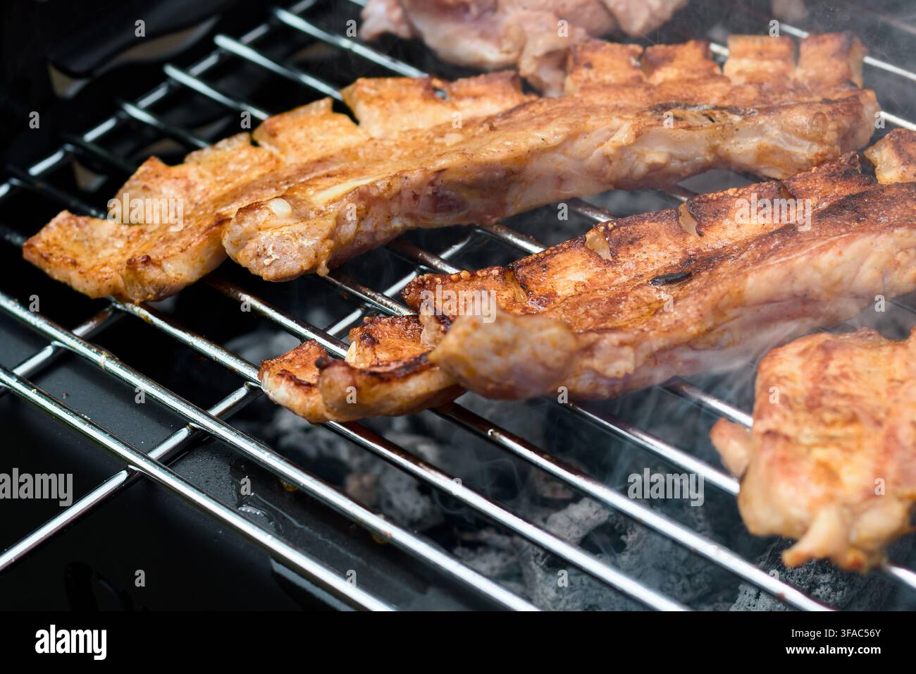 Fette di pancetta di maiale appetitose arrosto lentamente alla perfezione su un barbecue a carbonella con fumo fragrante che si alza dalle braci calde durante la cottura nel cortile Foto Stock