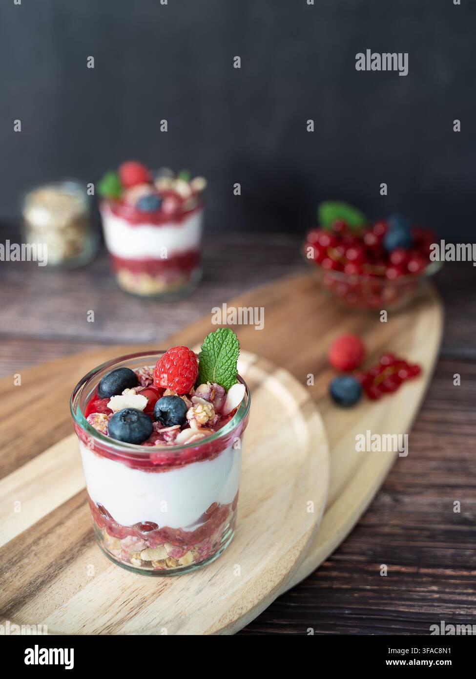 Dessert a strati con bacche di yogurt e granola croccante, stilizzato con oggetti rustici Foto Stock