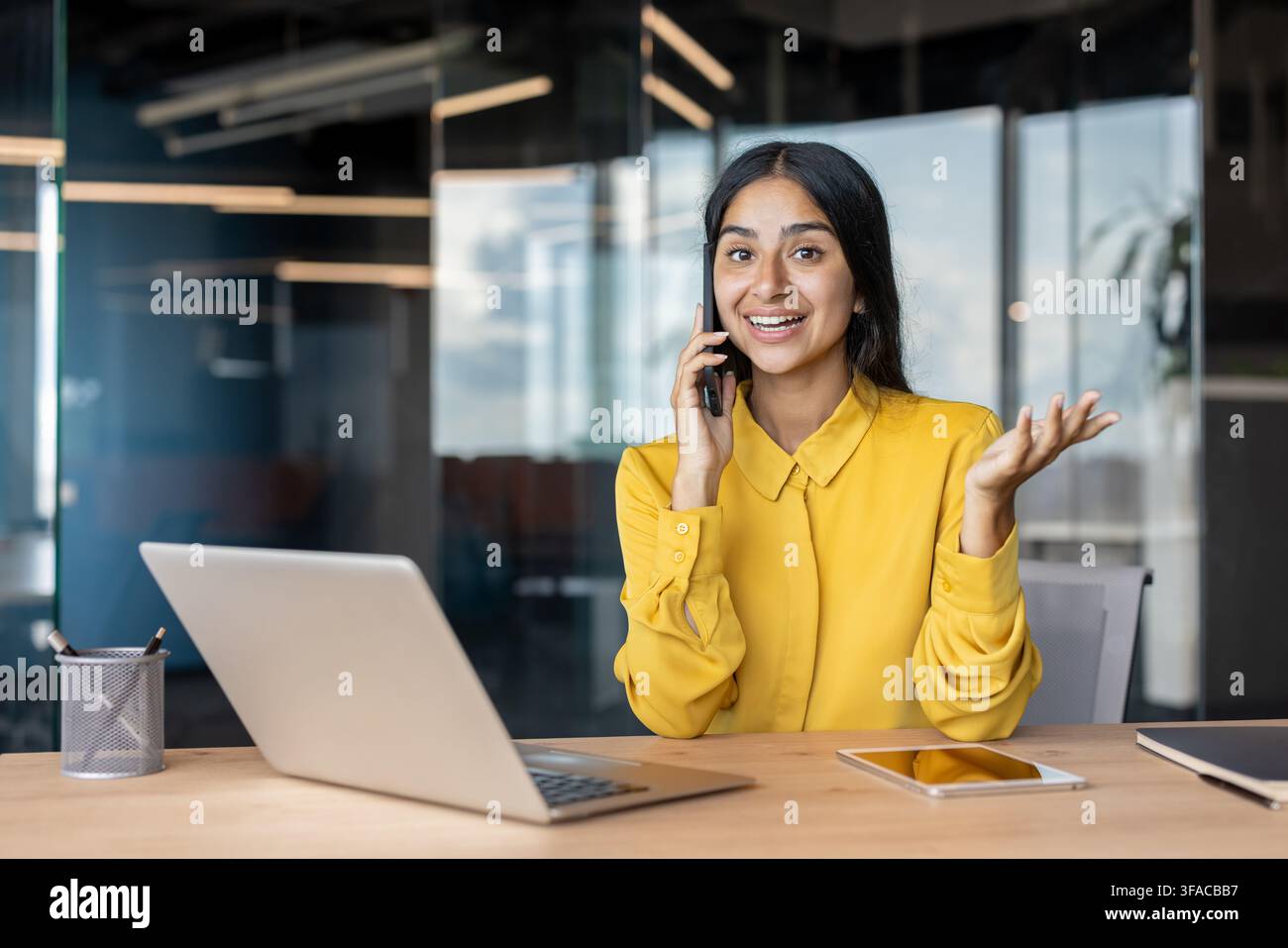 Giovane donna d'affari sorridente seduta alla scrivania in ufficio e al telefono. Foto Stock