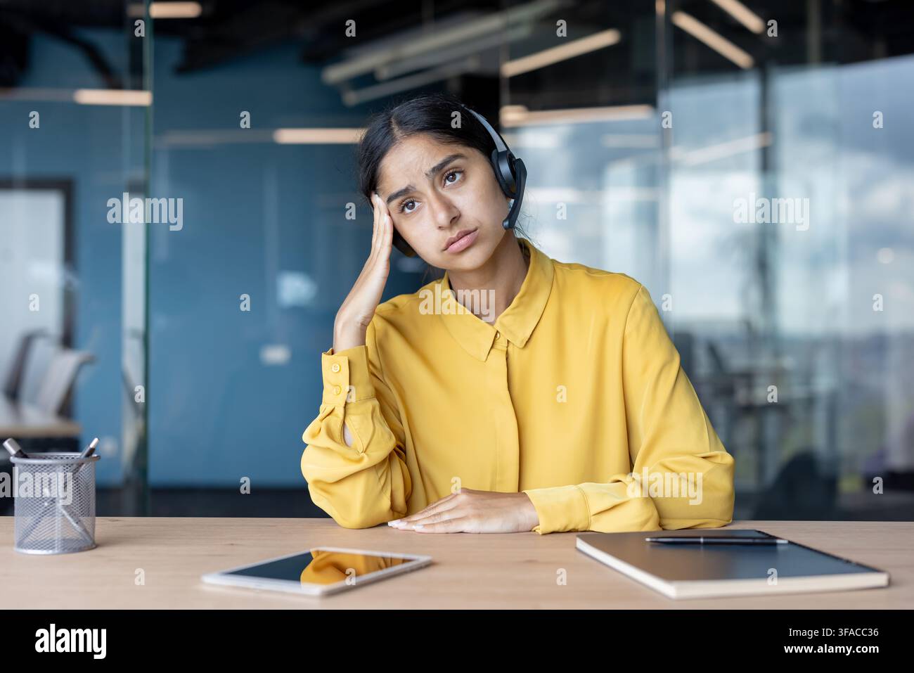 Giovane donna indiana stanca in abito seduta a una scrivania in ufficio e che tiene la testa. Foto Stock