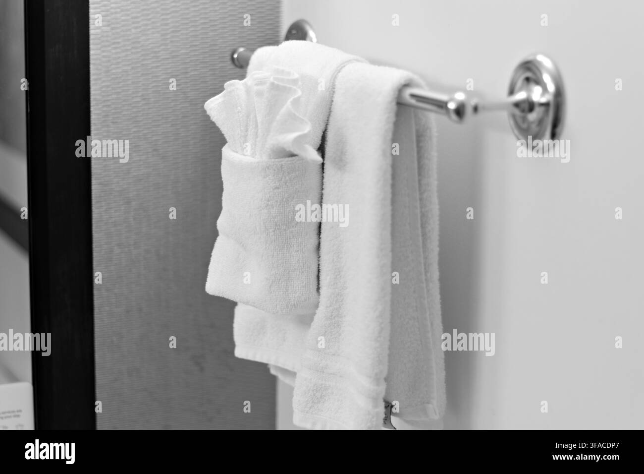 Asciugamani bianchi appesi ordinatamente su un elegante portasciugamani di metallo. Struttura di cotone morbido visibile sotto una luce delicata. Design minimalista per il bagno con linee pulite e neu Foto Stock