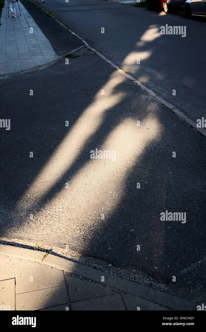Modelli di ombre geometriche e luce intensa proiettati sull'asfalto scuro di una strada pavimentata, contrasto netto tra le zone illuminate e il profondo Da Foto Stock