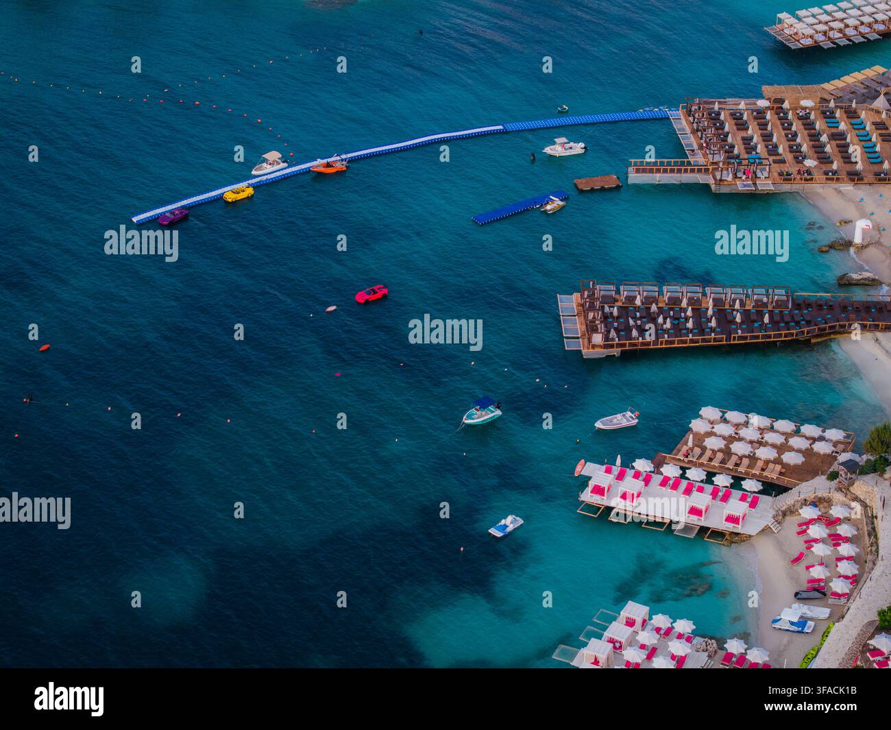 Vista aerea di club sulla spiaggia con piattaforme in legno, lettini e ombrelloni lungo la costa turchese a Ksamil, nella contea di Vlorë, Albania. Foto Stock