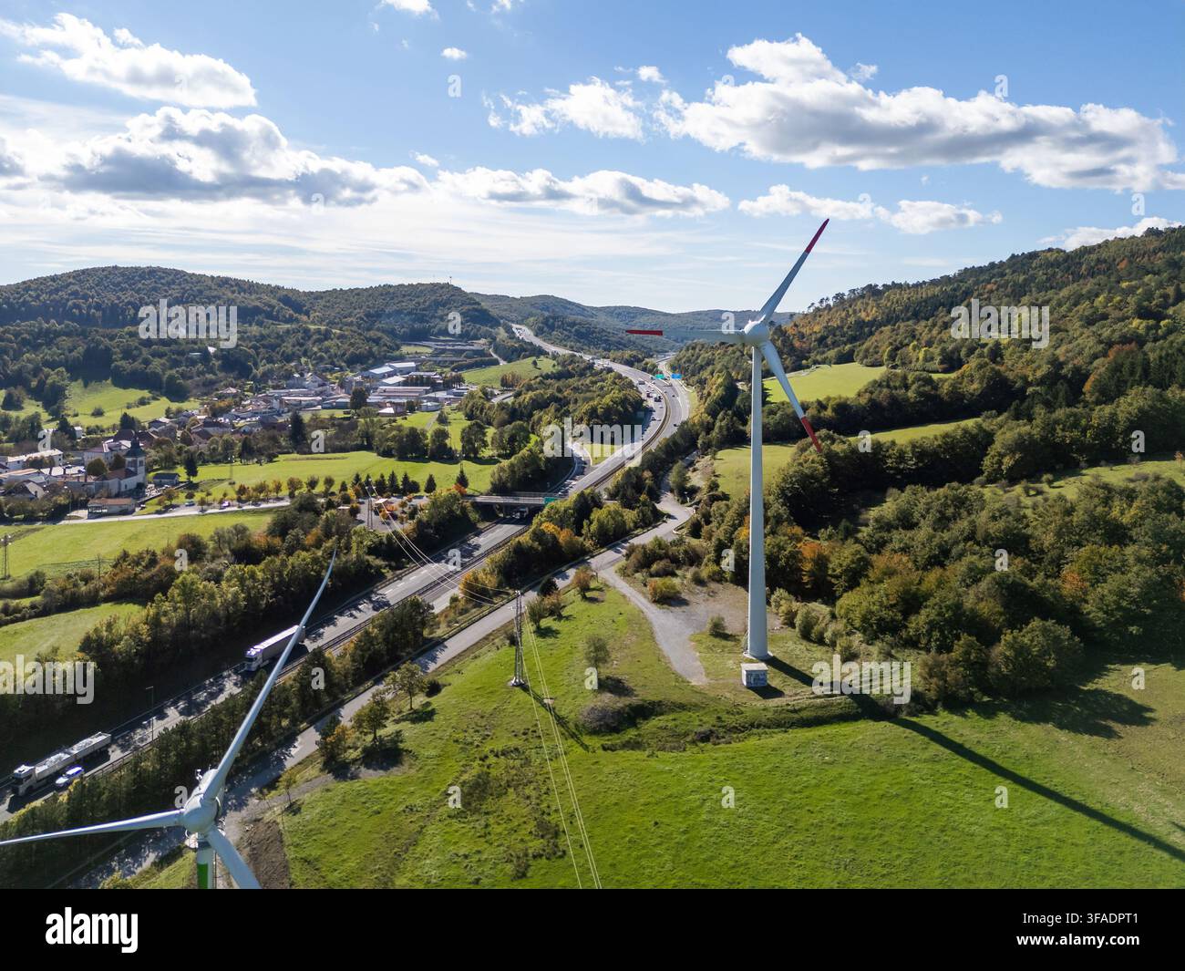 Una turbina eolica si trova vicino a un'autostrada trafficata con auto che si muovono lungo la strada. La scena unisce energia rinnovabile con mobilità moderna. Foto Stock