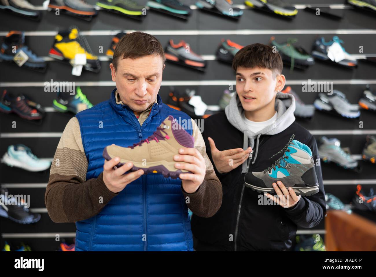 Padre e figlio insieme scelgono e acquistano scarpe per sport invernali per escursioni in negozio Foto Stock